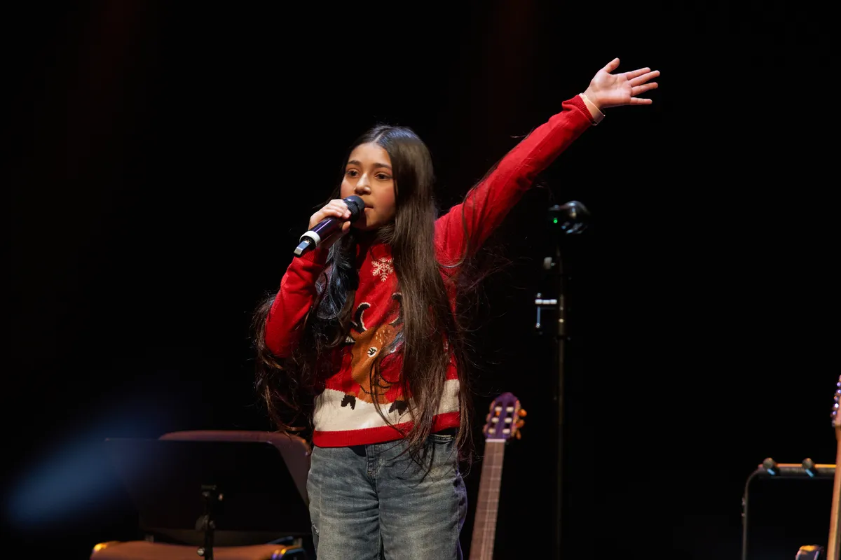 Jovem cantora de braço no ar no Recital de Natal de 2024